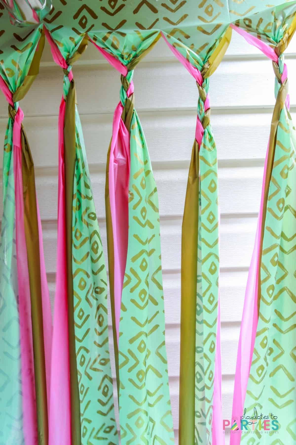 party backdrop made with a gold plastic tablecloth, a pink plastic tablecloth, and a patterned gold and aqua plastic tablecloth