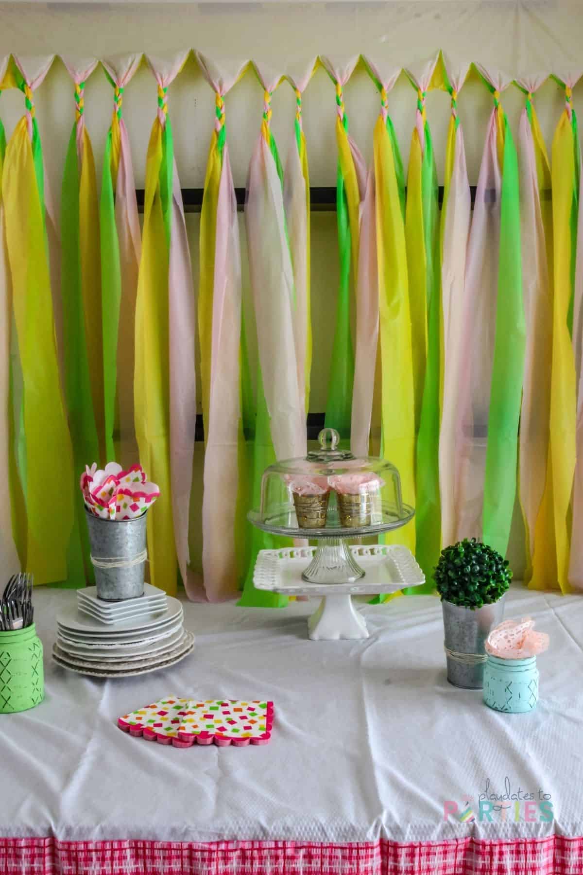 table with party supplies on it in front of a curtain made from braided tablecloth strips