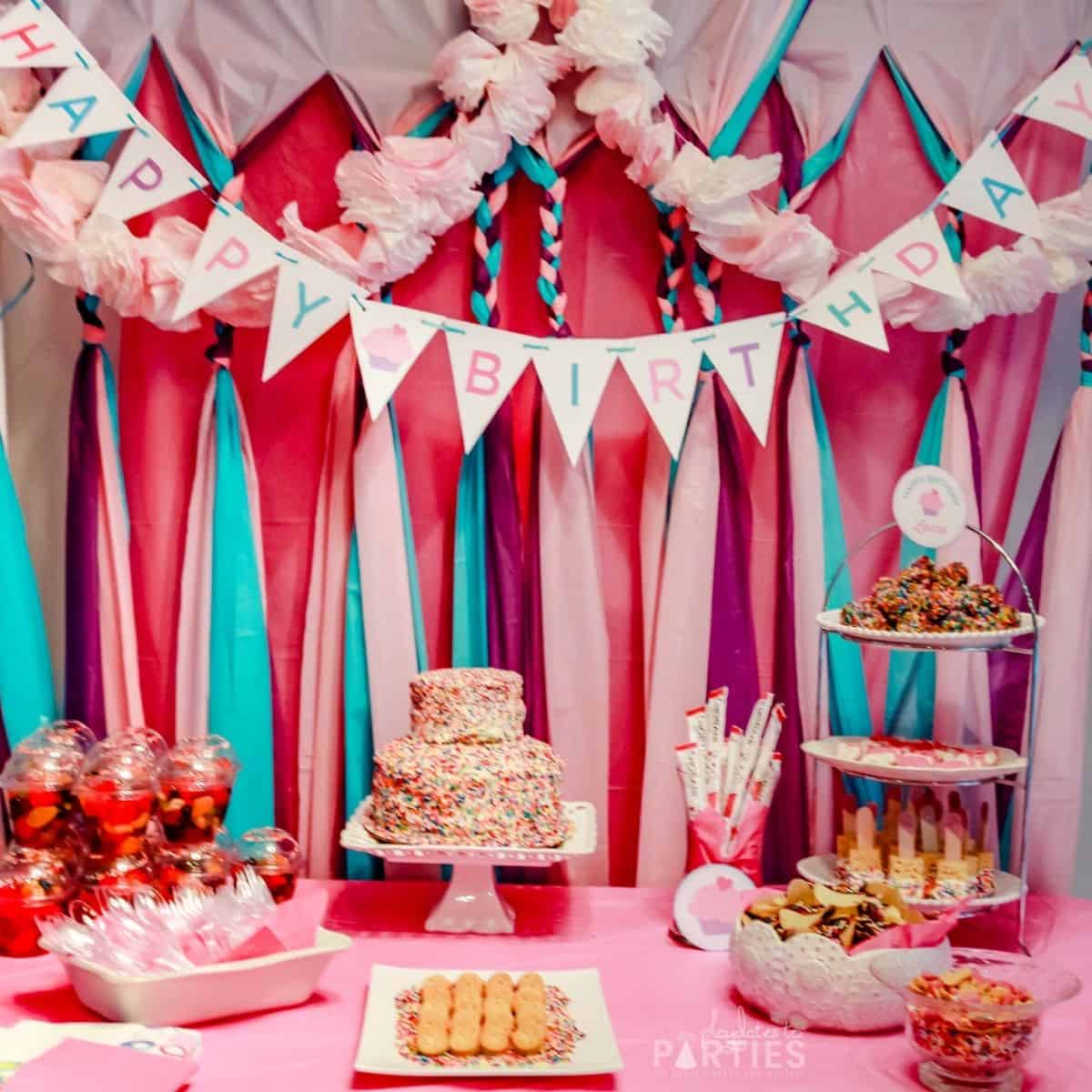 Photo of a party setup with a tricolor backdrop, fluffy garland, birthday banner, and snacks on the table