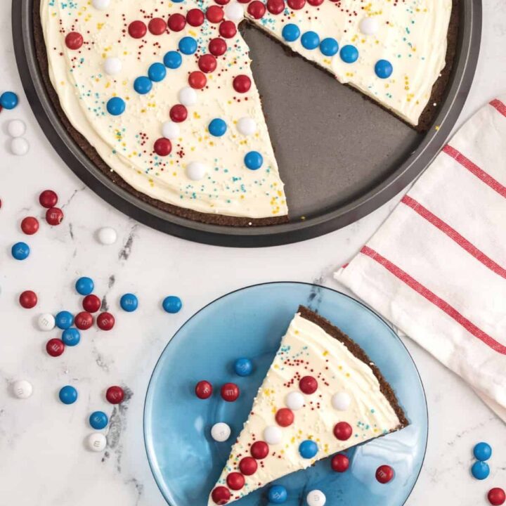 Overhead view of a July 4th dessert pizza with a slice cut out and on a blue plate.