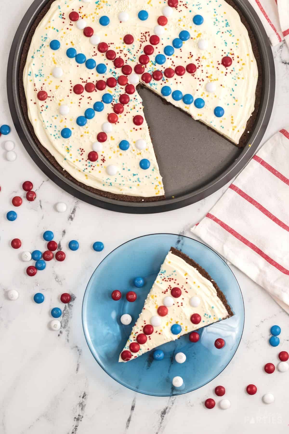 Overhead view of a July 4th dessert pizza with a slice cut out and on a blue plate.