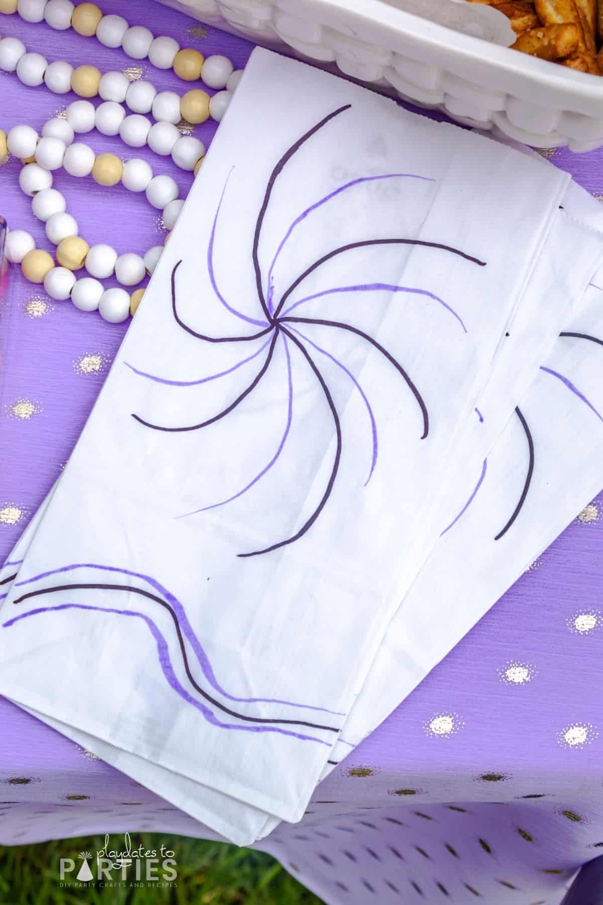 close up of white paper bags hand decorated with black and purple swirls