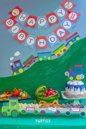 A train birthday party buffet with a variety of themed party food, a happy birthday banner, and other DIY decor