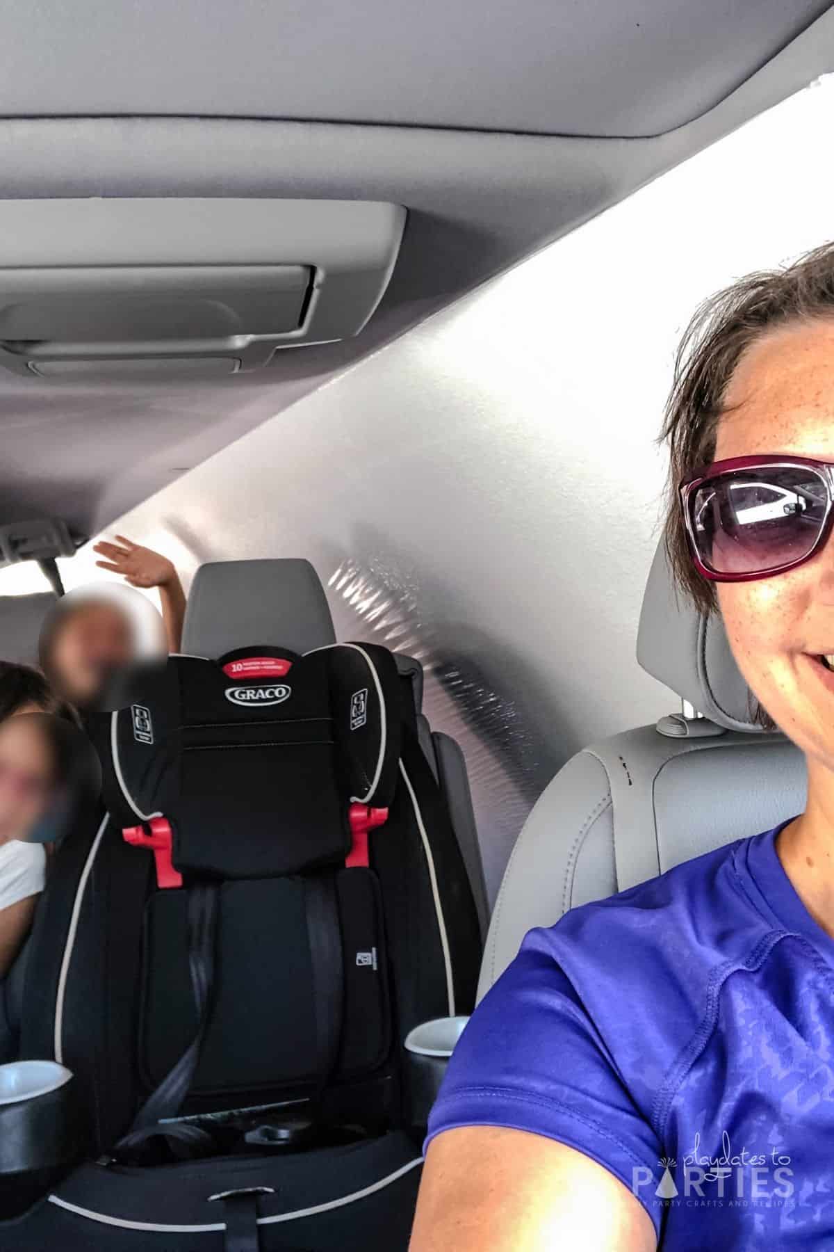 image of woman in a car with a large white board inside and two children riding in the back