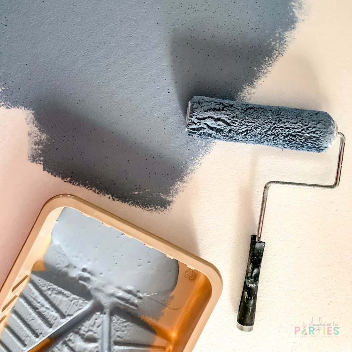 a styrofoam board partially painted blue with a paint roller and paint pan on top