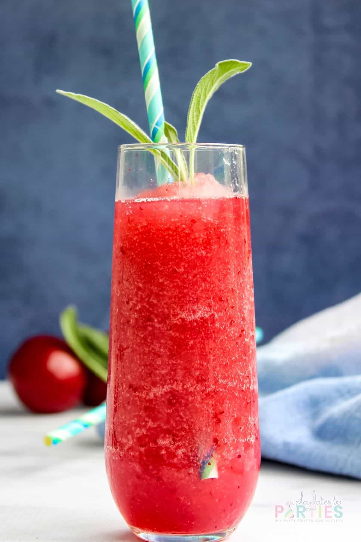 Close up view of a finished blueberry wine slushie with plums garnished with basil and a paper straw