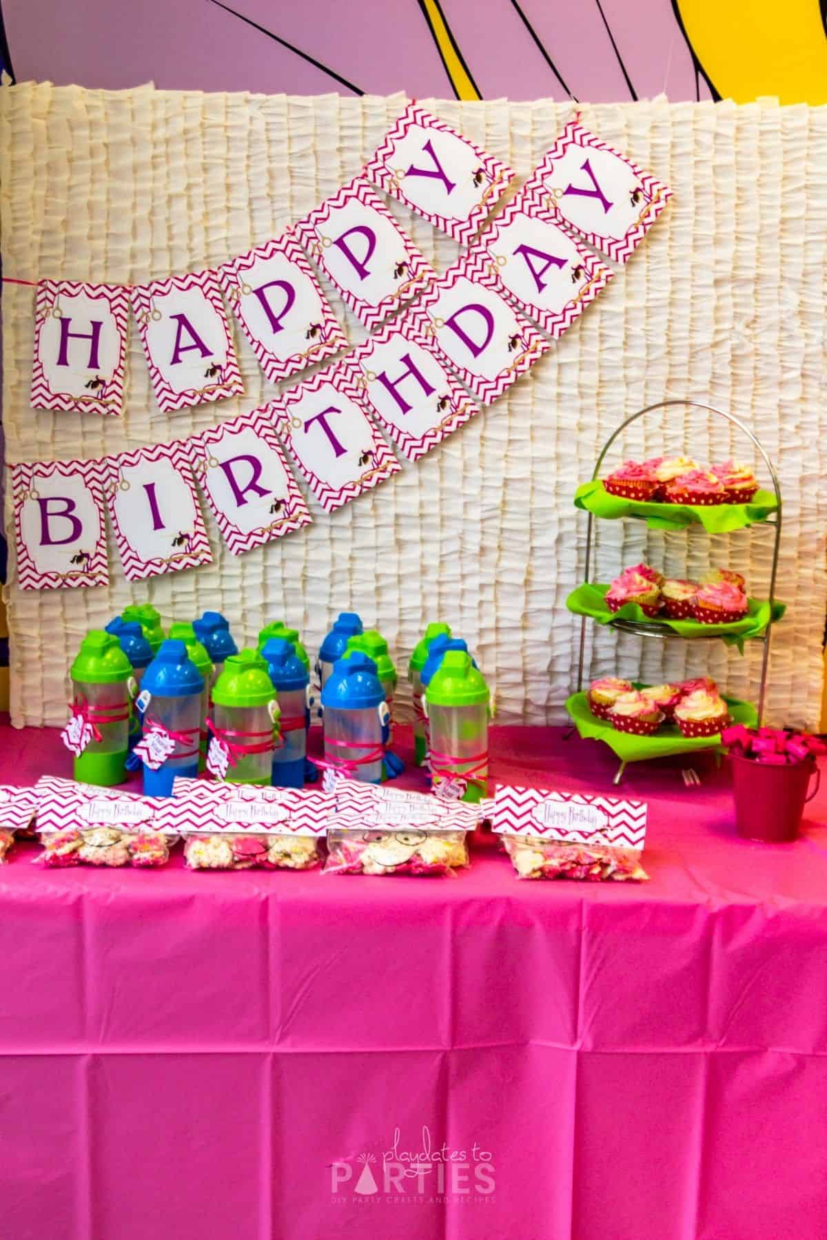 Favor and dessert table with a ruffled backdrop and a gymnastics party banner that says Happy Birthday