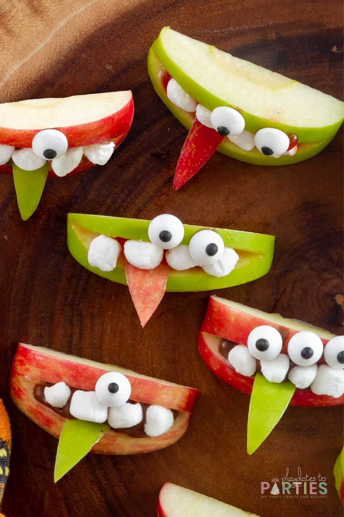 Overhead view of green and red apple wedges decorated with marshmallow teeth and candy eyeballs to look like cute monsters.