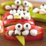 Close up front view of an apple wedge decorated to look like a cute Halloween monster.
