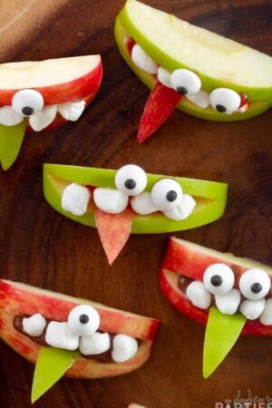 Overhead view of green and red apple wedges decorated with marshmallow teeth and candy eyeballs to look like cute monsters.