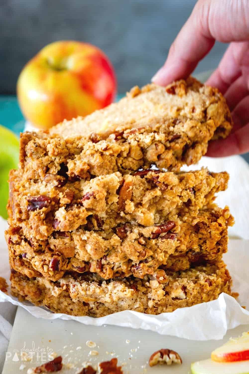 A woman's hand grabbing a slice of apple bread from a stack of slices.