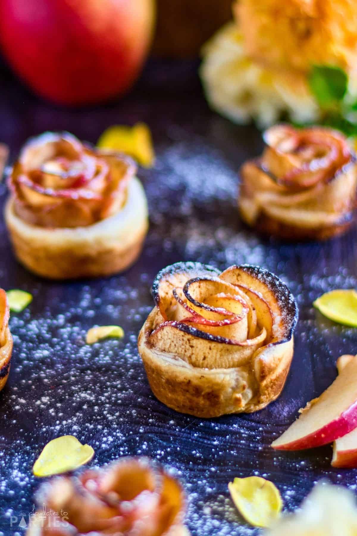 Mini apple tarts on a dark surface surrounded by flower petals