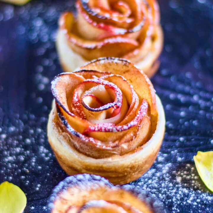 close up of four finished apple roses with puff pastry dusted with powdered sugar