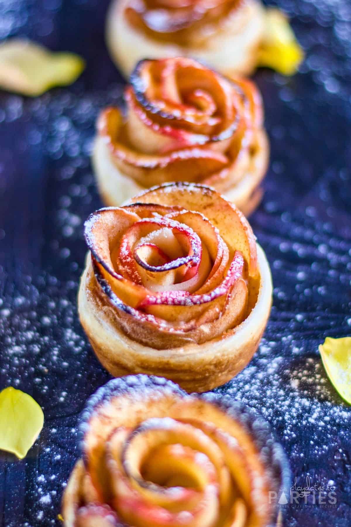 close up of four finished apple roses with puff pastry dusted with powdered sugar