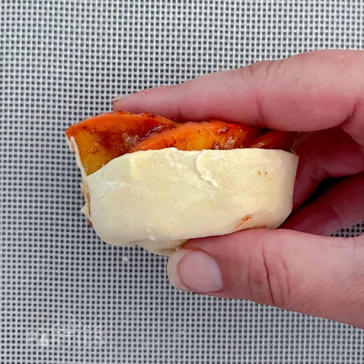 close up of a woman's hand holding apple slices in place while rolling a rosette