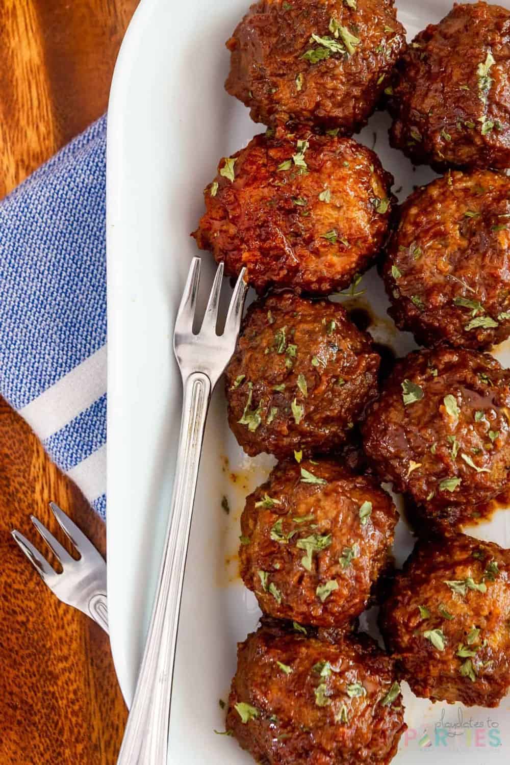 cocktail meatballs arranged on a white plate with cocktail forks laying nearby