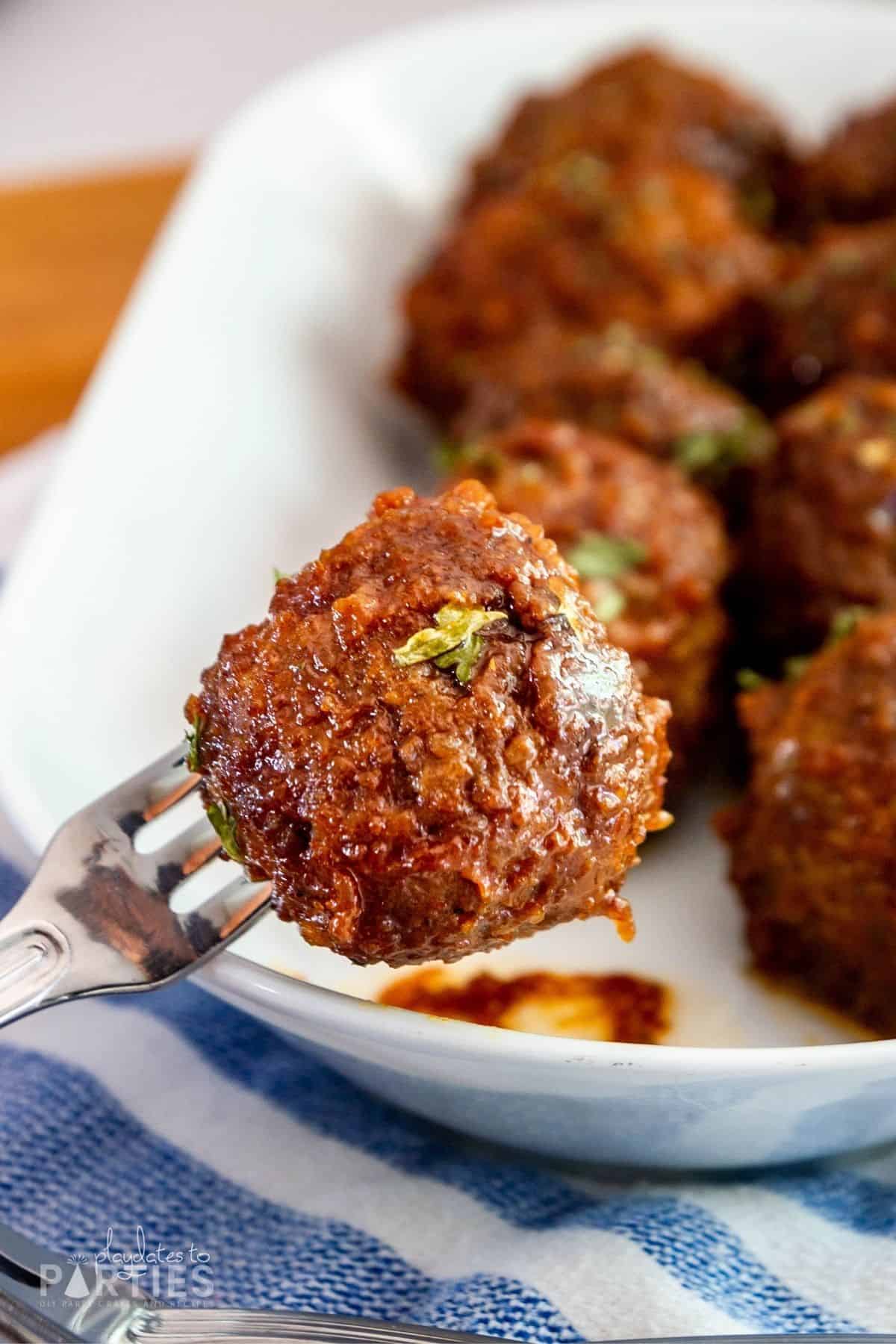 close up of a meatball on a cocktail fork with a plate of meatballs in the background