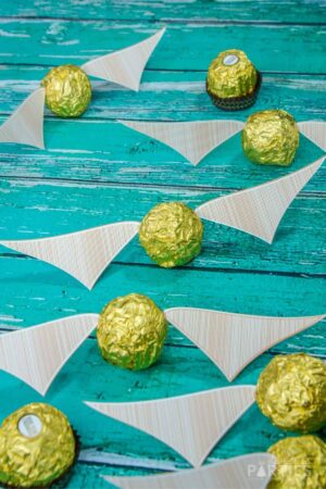 Ferrero Rocher golden snitch's scattered on a blue table with printed wings attached.