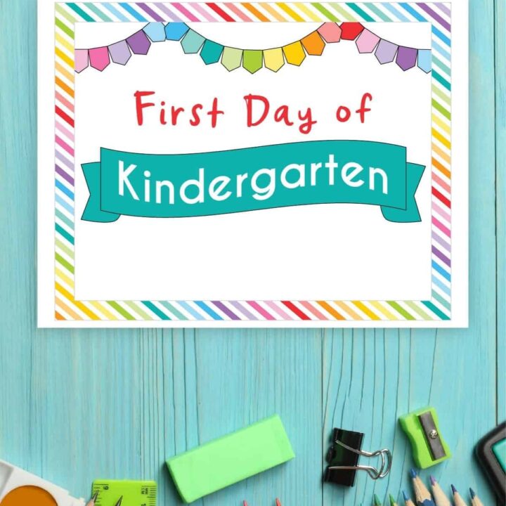 Mock up of a printable sign that says First Day of Kindergarten, surrounded by school supplies on a blue table.