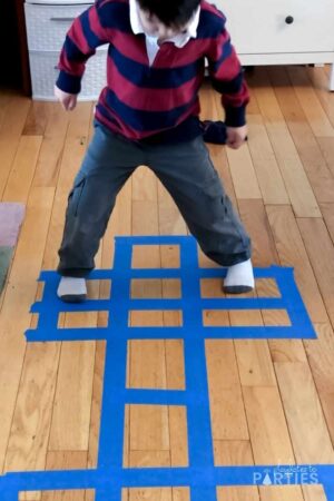 photo of a young boy playing hopscotch indoors on a wood floor with a taped course