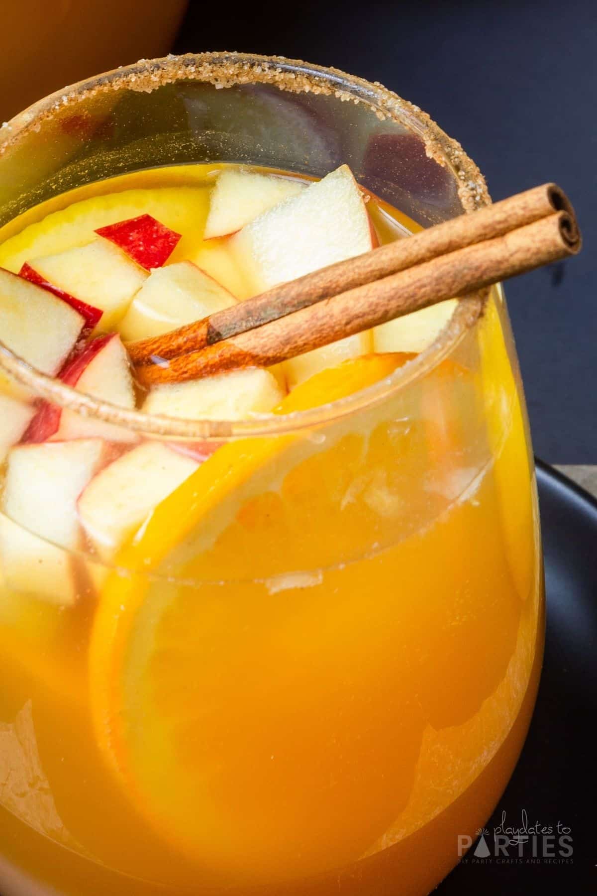 Close up of a glass of sangria with a cinnamon sugar rim and garnished with a stick of cinnamon.