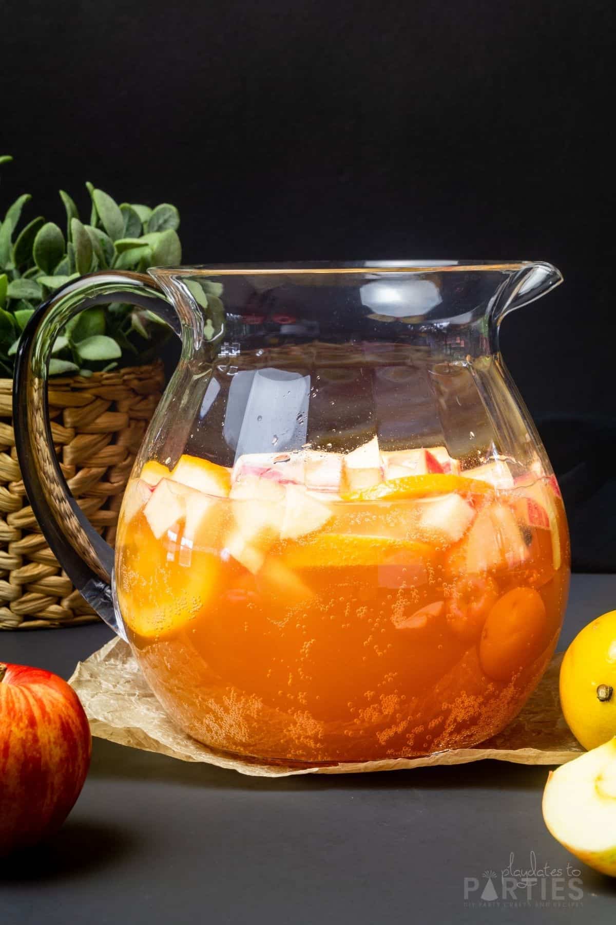 A pitcher filled with apple cider sangria surrounded by apples and lemons.