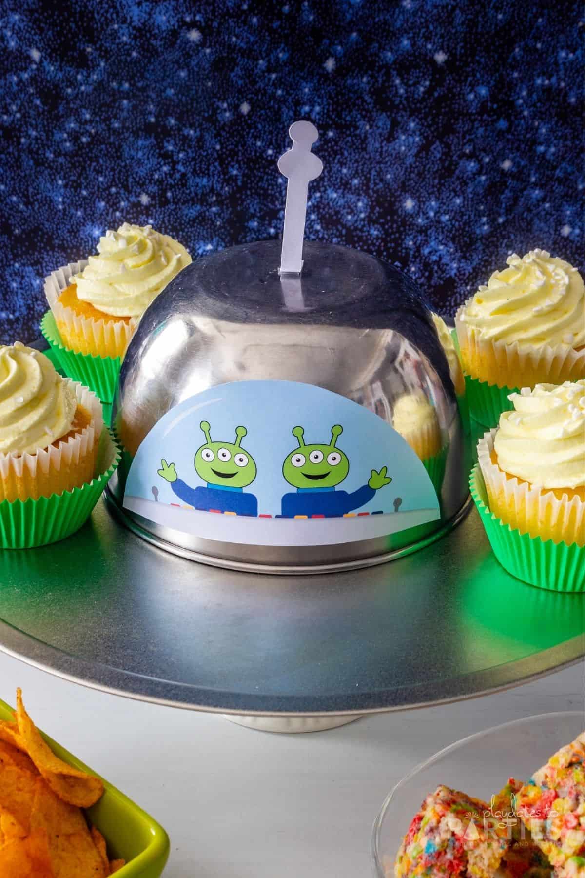 Slightly overhead view of space themed party tray surrounded by cupcakes with green liners.