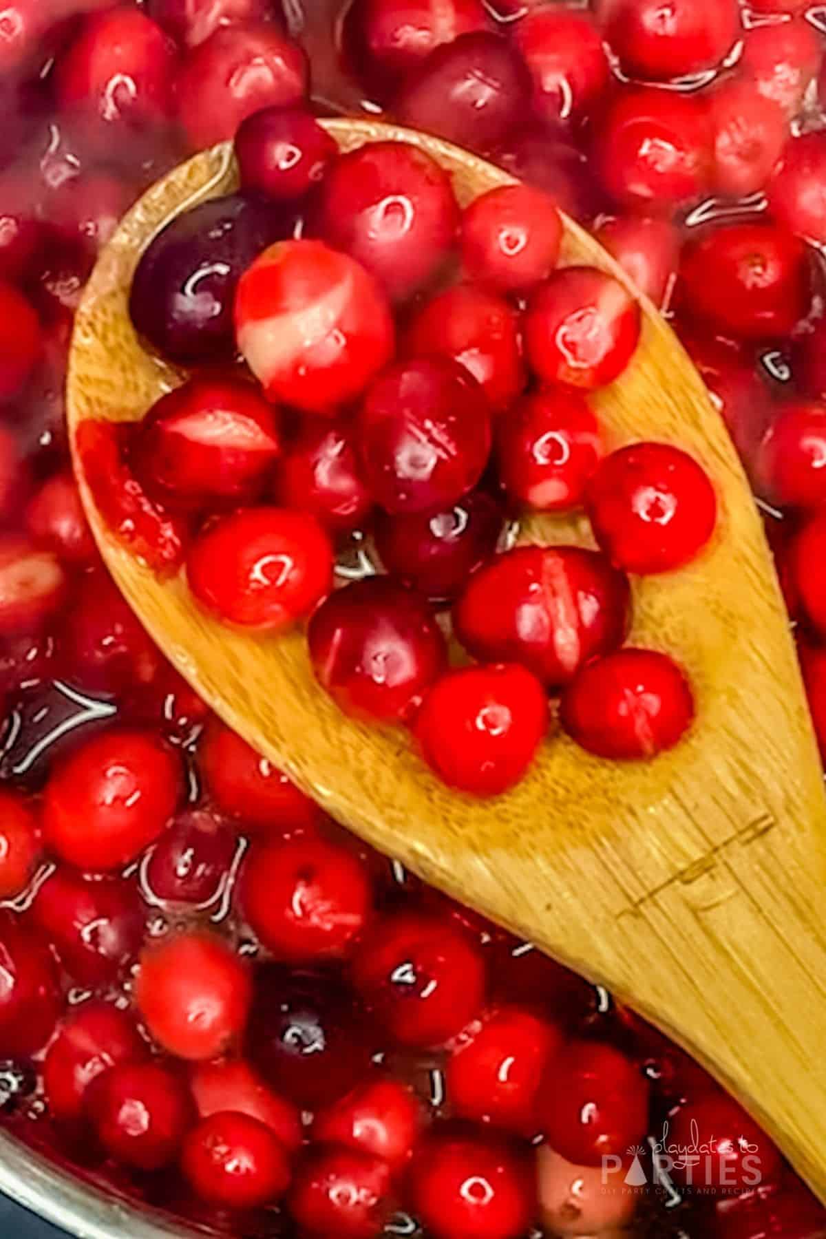 A wooden spoon with cranberries, some of which have popped.