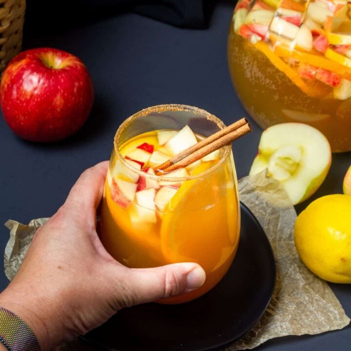 A woman's hand grabbing a glass of spiced apple cider sangria.