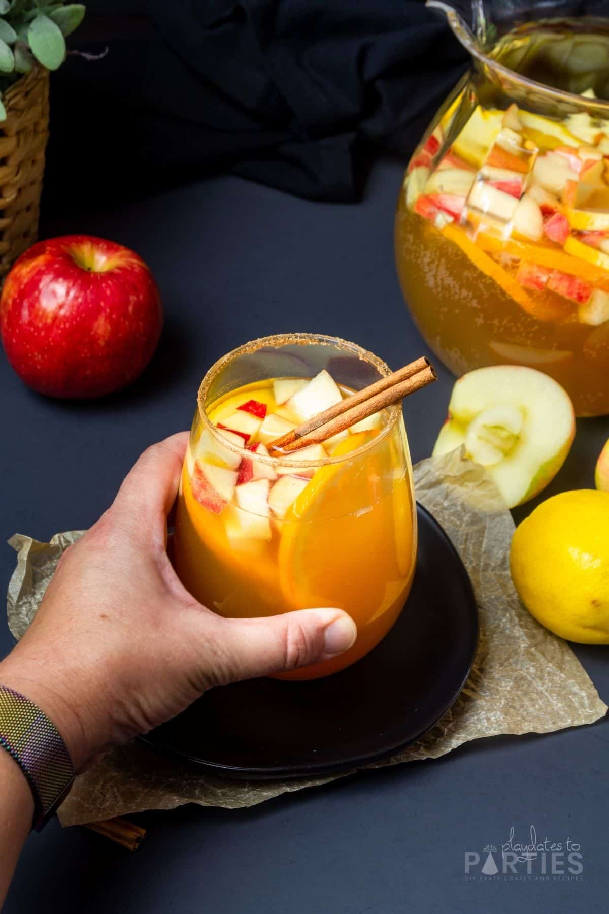 A woman's hand grabbing a glass of spiced apple cider sangria.