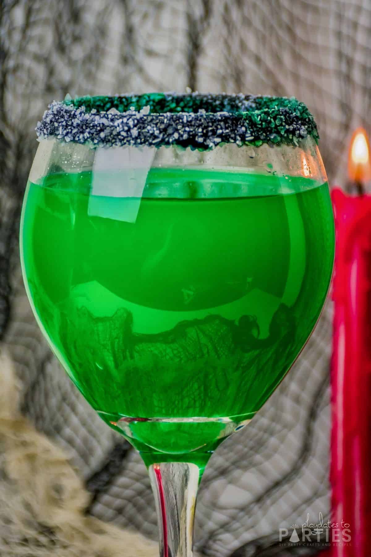 Front view of a large wine glass filled with a green Halloween cocktail.