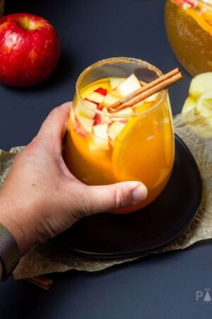 A woman's hand grabbing a glass of spiced apple cider sangria.