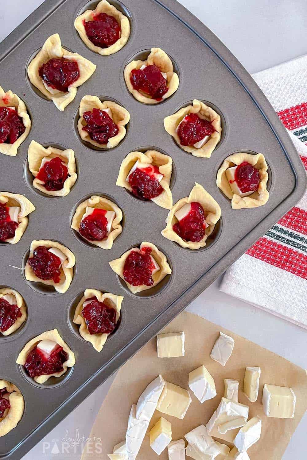 Overhead view of a mini muffin tin prepared with crescent roll dough, cheese, and jelly.