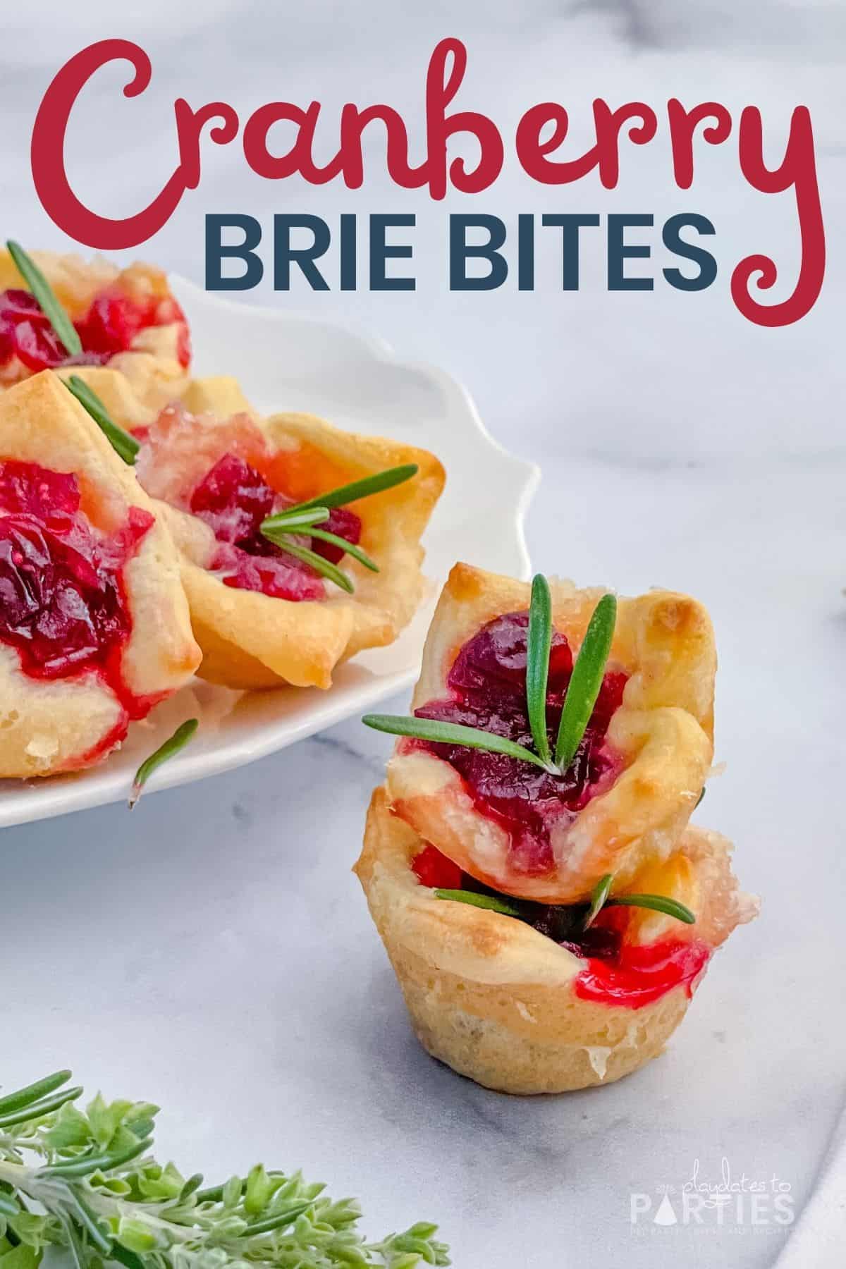 Cranberry brie bites stacked on a marble surface with a plate of brie bites in the background.