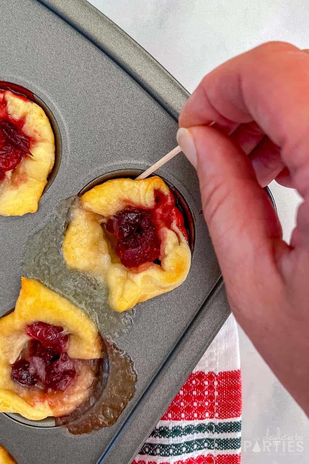 A woman's hand using a toothpick to remove an appetizer from a mini muffin tin.