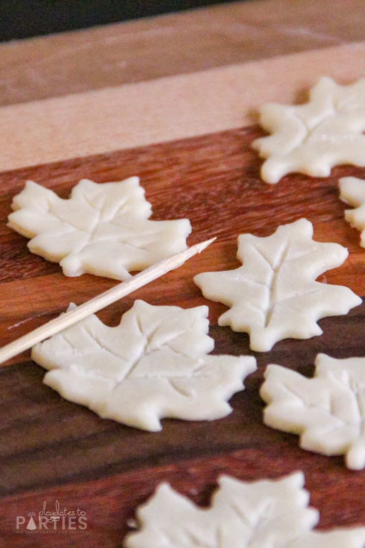 Leaf shaped pie crusts on a cutting board with a wooden skewer nearby.