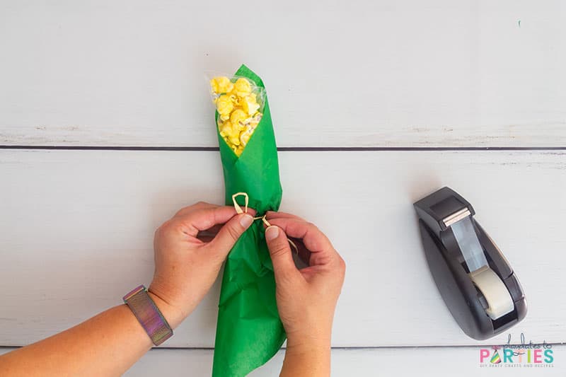 Tying the raffia ribbon on the popcorn corn on the cob favor.