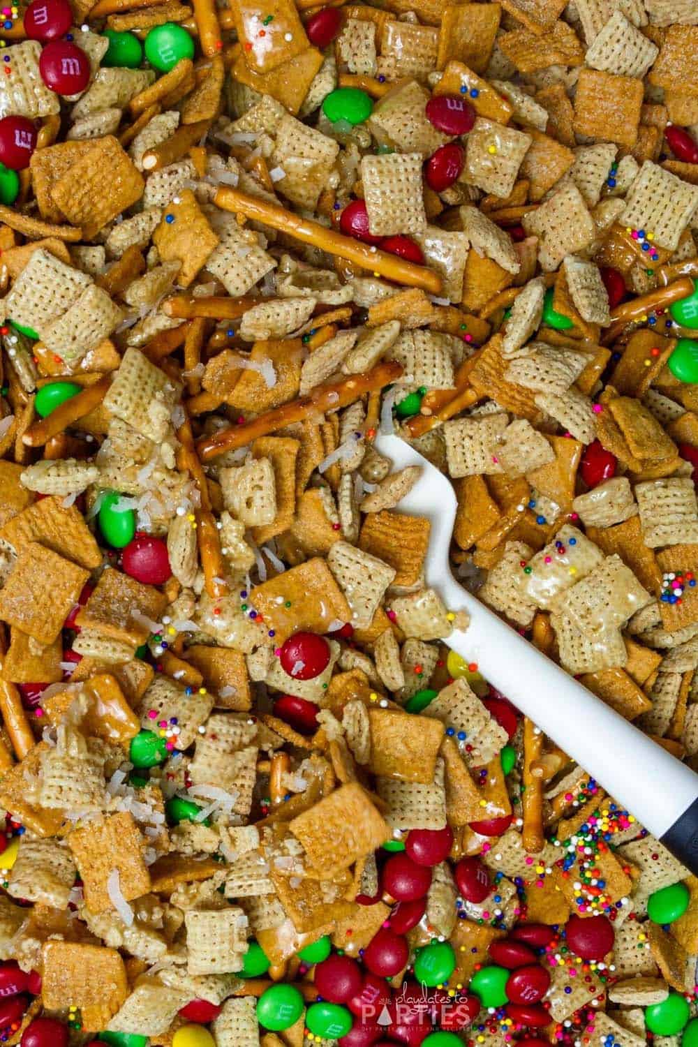 Overhead image of Chex Mix Christmas crack candy spread out on a pan with a spatula in the center.