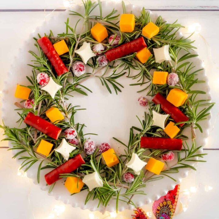 A Christmas appetizer wreath on a white plate with Christmas lights underneath the plate.