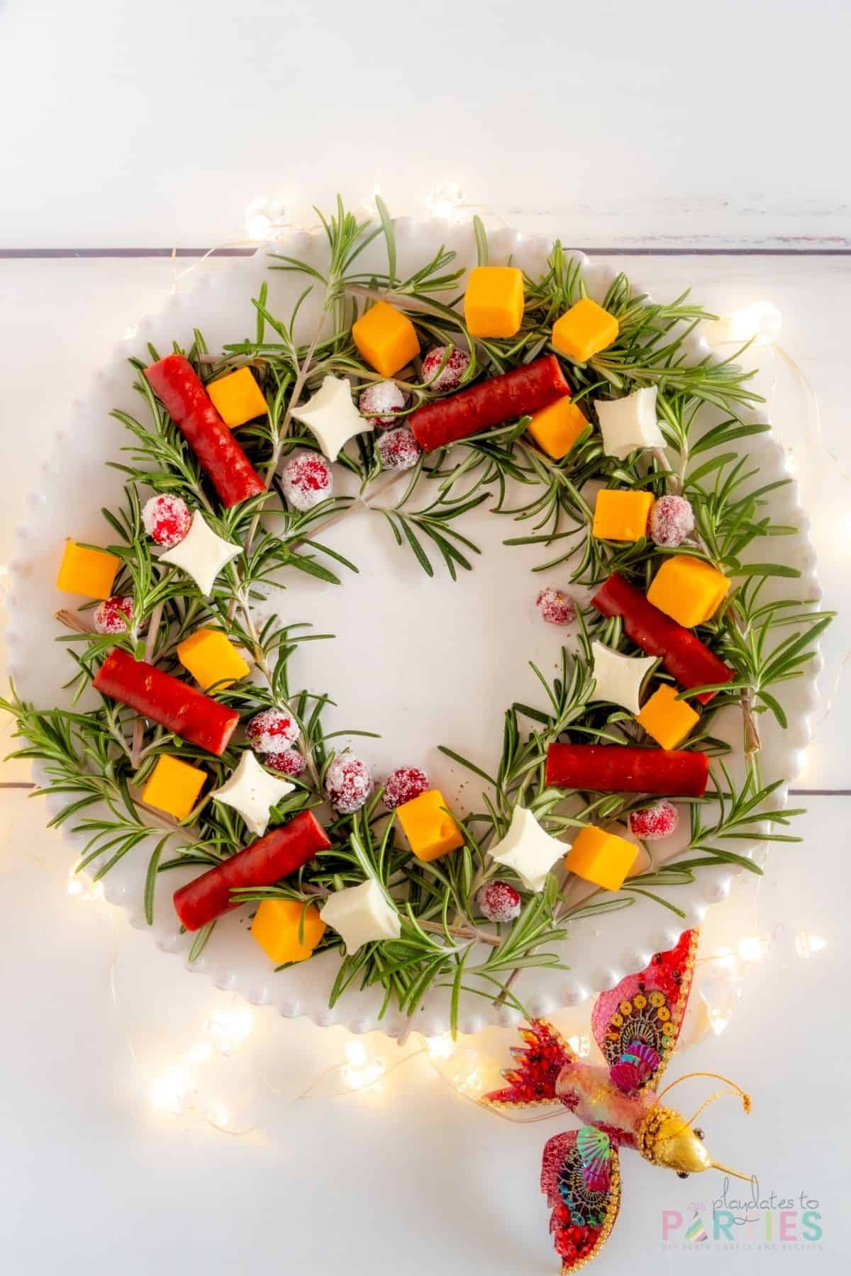 A Christmas appetizer wreath on a white plate with Christmas lights underneath the plate.