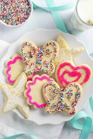 Sugar cookies on a plate decorated with icing and colorful sprinkles.