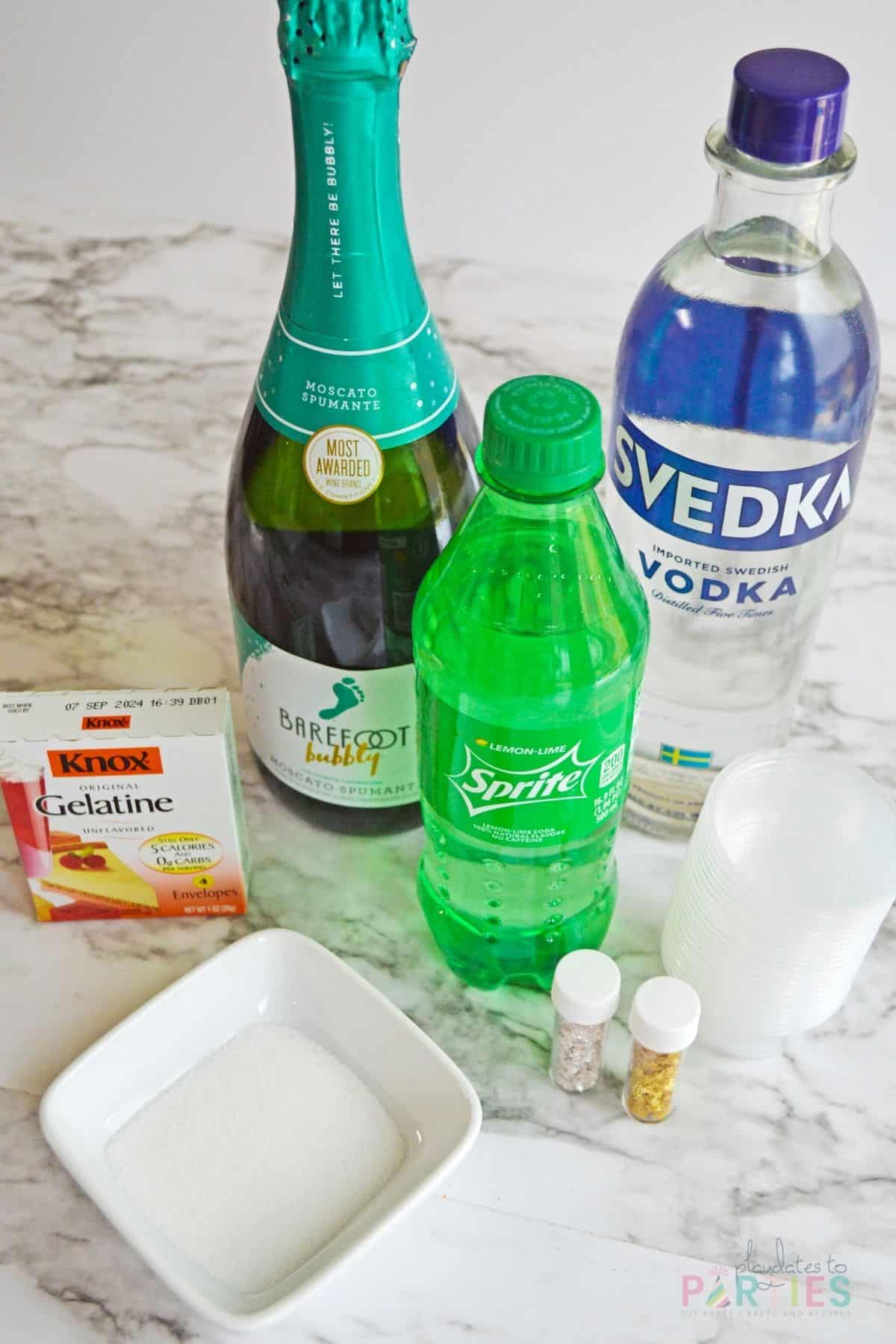 Ingredients on a marble surface - Champagne, vodka, gelatin, Sprite, sugar, and sprinkles.