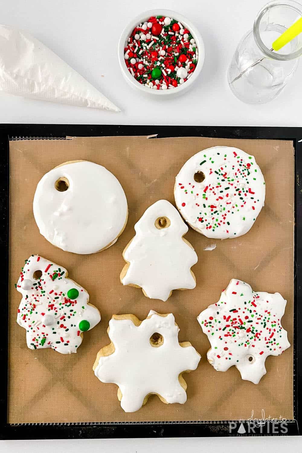 Cookies on a baking mat surrounded by sprinkles and a piping bag.
