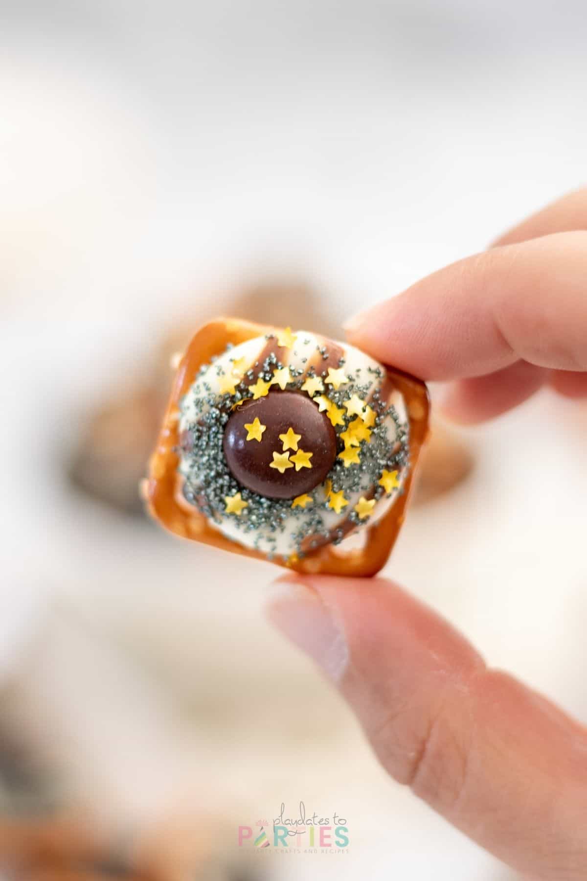 Close up of a woman's hand holding a pretzel with a Hershey's Hug, M&M, and holiday sprinkles.