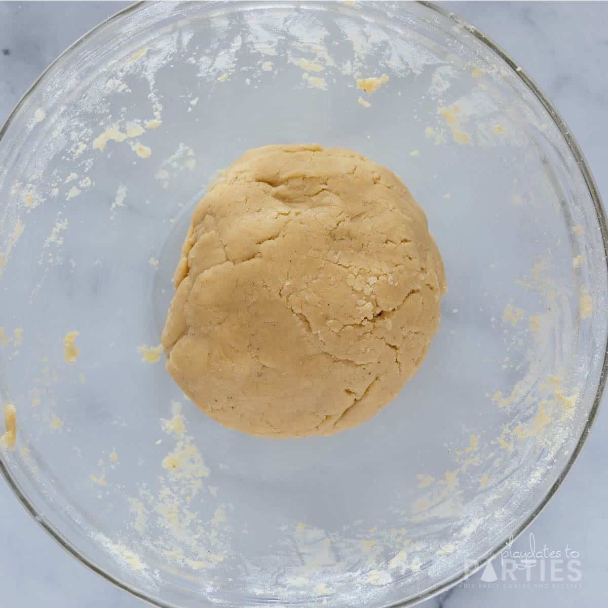 A ball of sugar cookie dough in a large glass bowl.