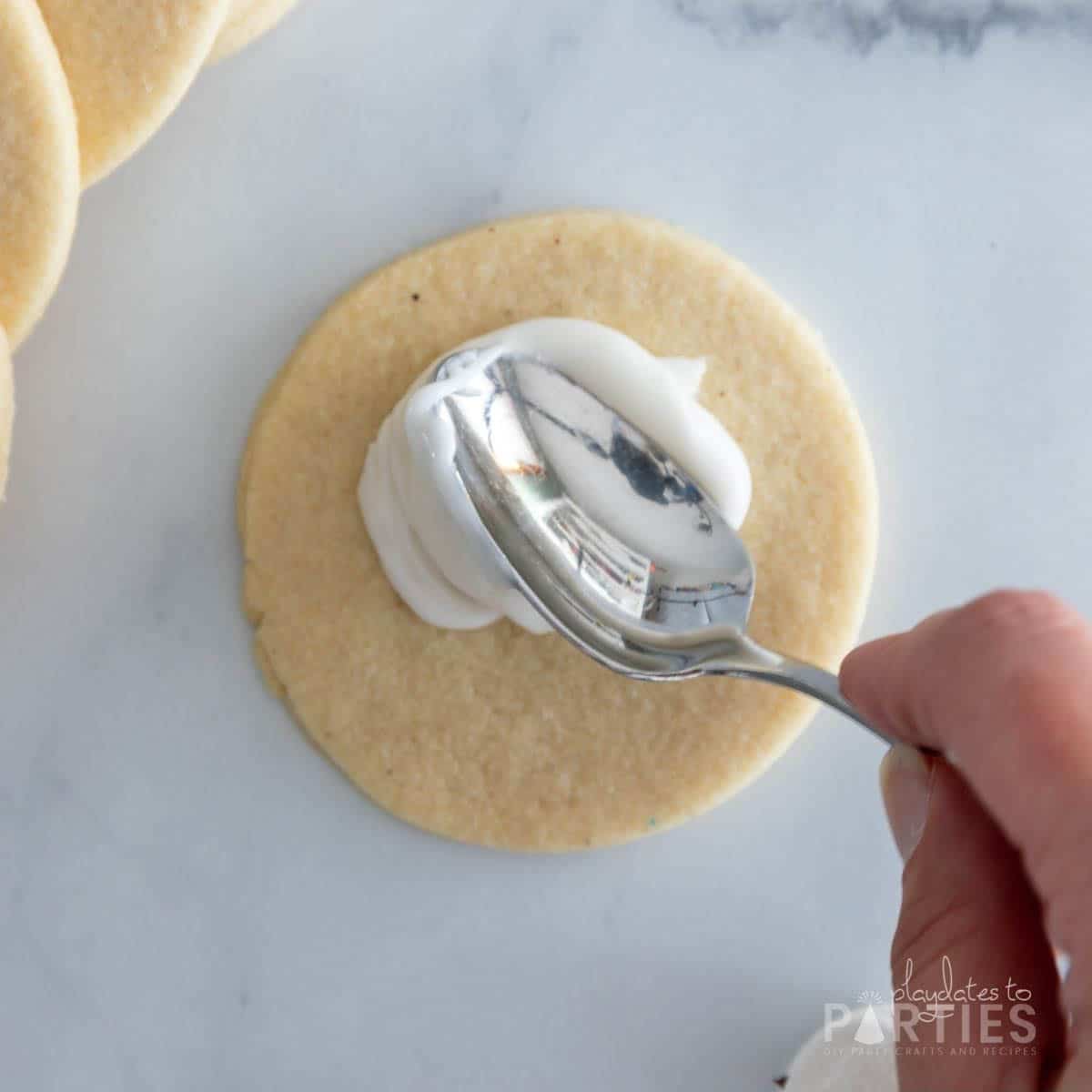A woman's hand spreading white icing onto a round sugar cookie.
