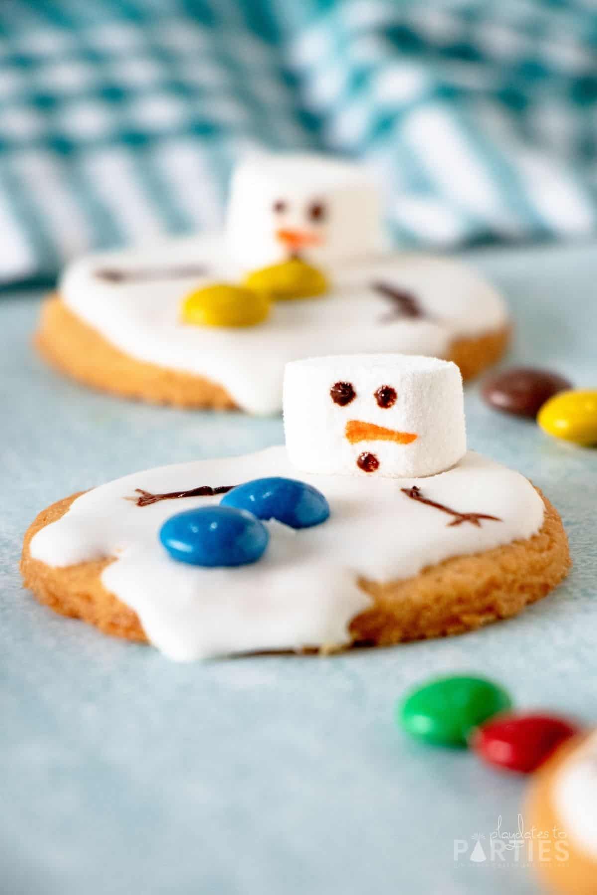 Close up view of a cookie decorated with white icing, blue M&Ms, and a marshmallow.