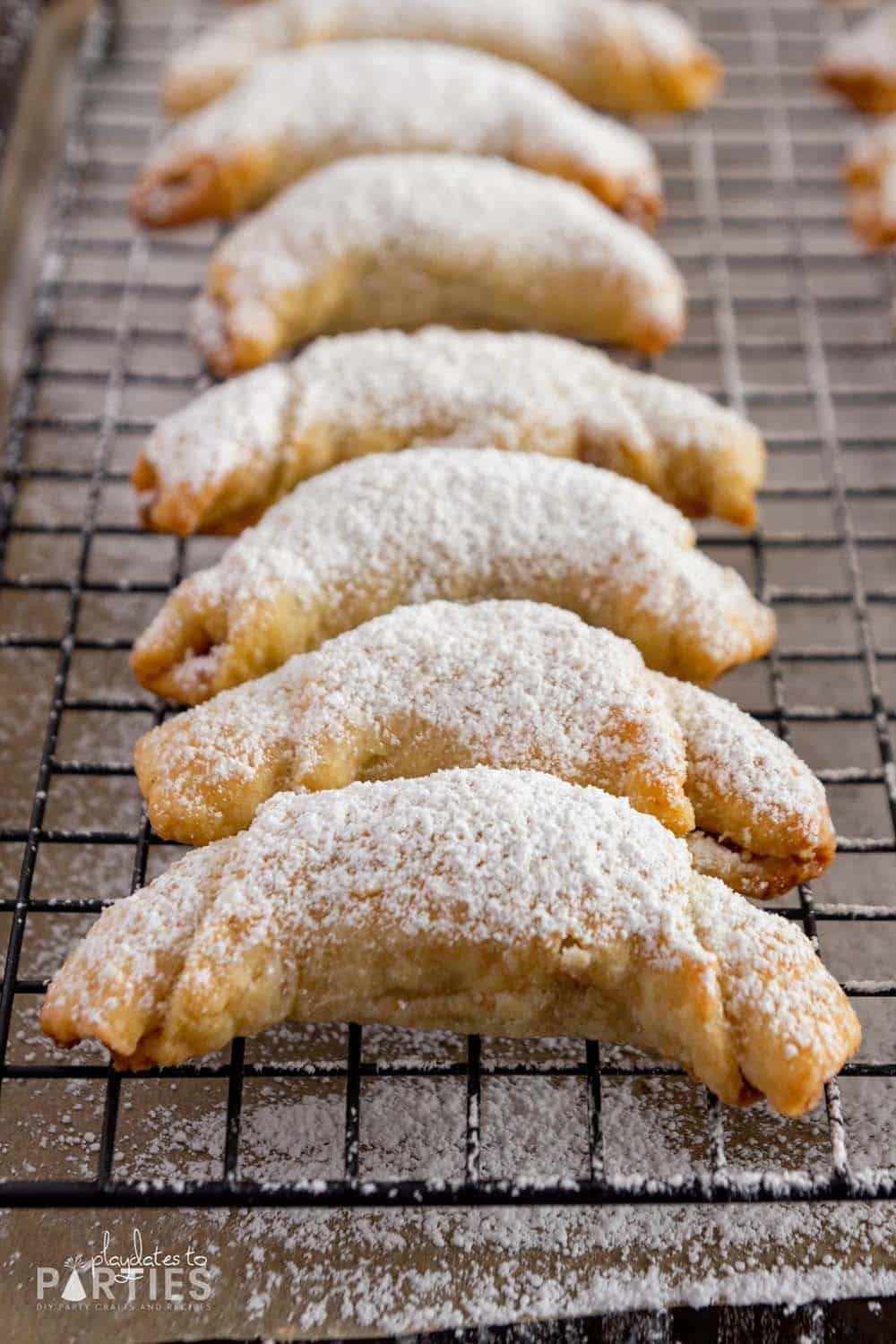 Baked pecan crescent cookies on a cooling rack dusted with powdered sugar.