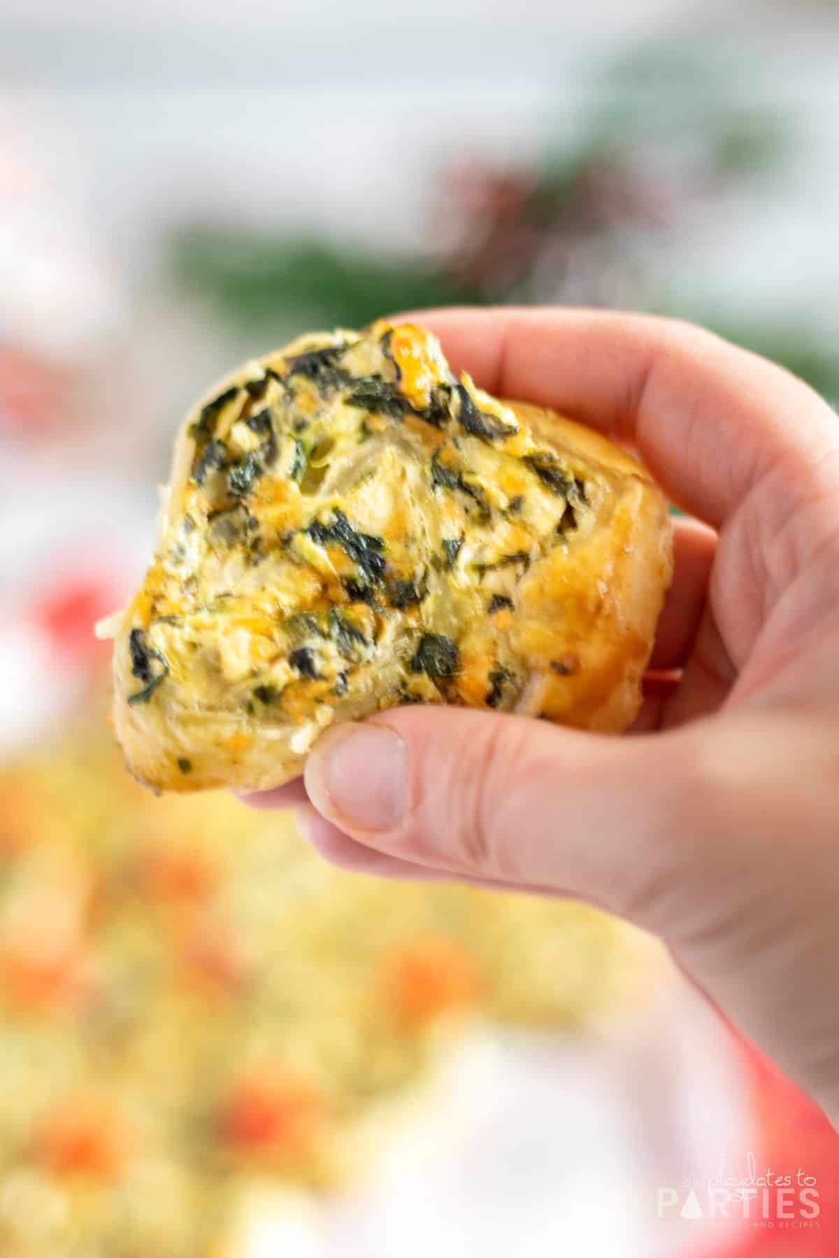 Close up of a woman's hand holding a puff pastry pinwheel with spinach filling.