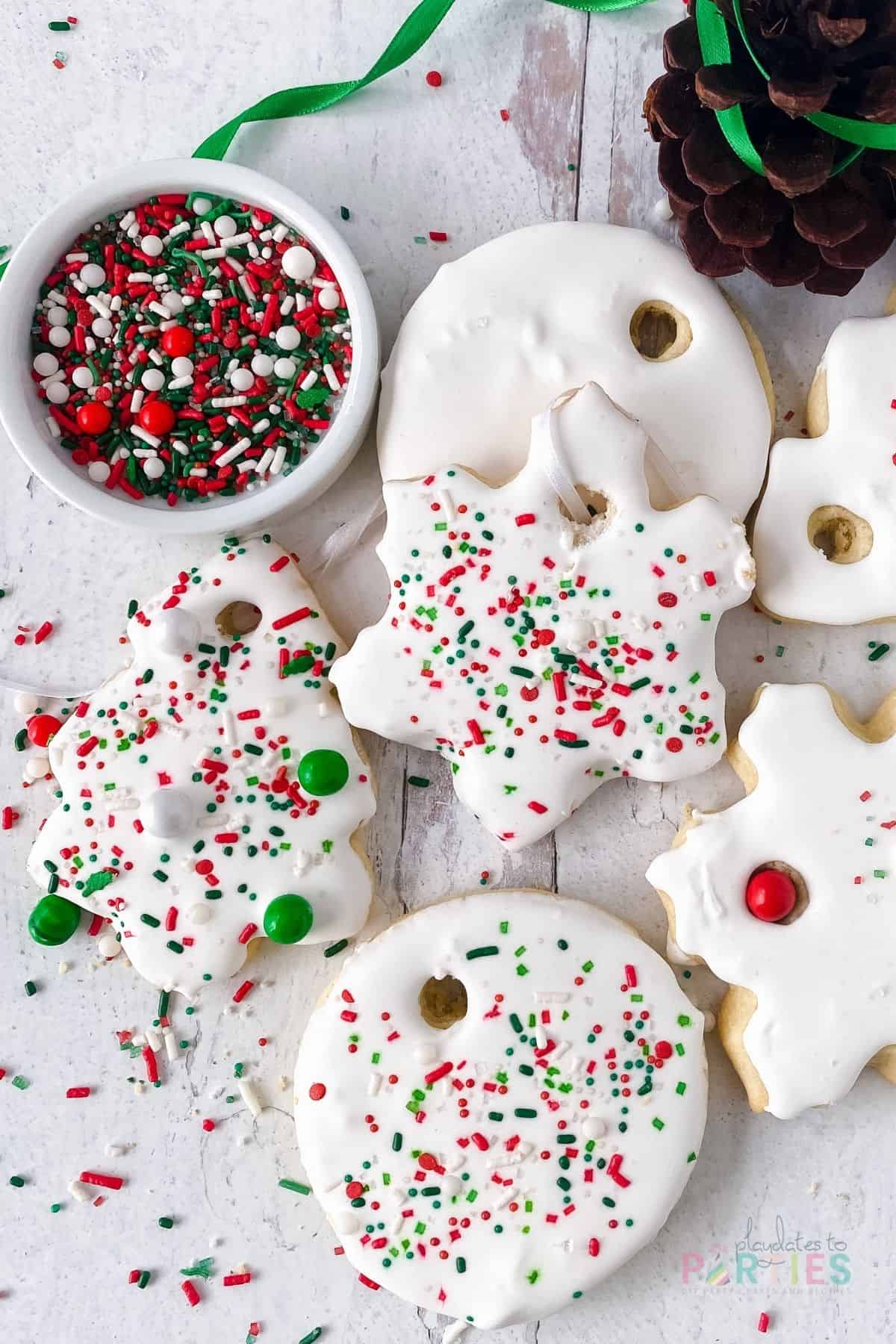 Sugar cookies decorated with white icing and holiday sprinkles on a white wood surface.